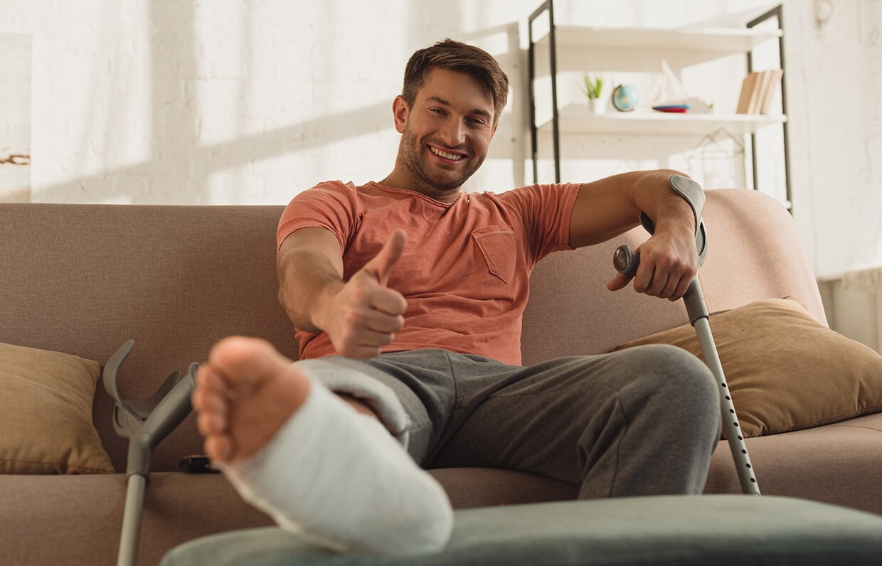 muž na pohovke so zlomenou nohou a barlami